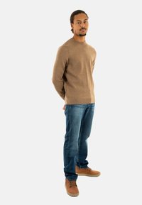 Maglione lavorato a maglia color tan, jeans in denim blu e scarpe con lacci marroni. Design aderente, polsini a coste e texture sul maglione.