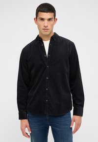 Schwarzes Cordhemd mit Knöpfen, Standardkragen und langen Ärmeln, mit geradem Saum und feiner Struktur. Kombiniert mit blauen Jeans.