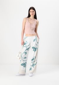Light pink ribbed crop top with a drawstring detail, paired with loose white pants featuring green floral prints. White sneakers and a small bag.