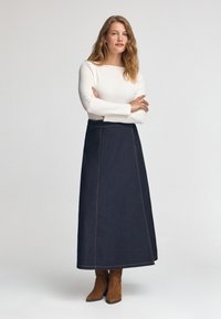 Mörk denim maxikjol med framträdande sömmar, bärs med en figurnära vit långärmad tröja och bruna mocka ankelstövlar.