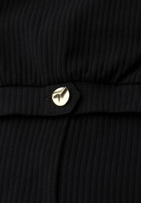 Close-up of black ribbed fabric with a gold, irregularly shaped button fastening a fabric strap.
