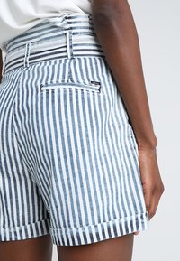 Szorty z paskami z materiału w pionowe niebiesko-białe paski, posiadające tylną kieszeń na zamek oraz wywinięty brzeg. Wykonane z lekkiego materiału.