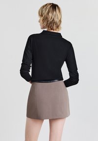 Haut noir à manches longues avec col, associé à une mini-jupe taupe. Le tissu semble lisse avec une silhouette ajustée.