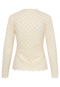 Haut en dentelle à manches longues couleur crème avec motif festonné et ourlet festonné, présenté de dos sur fond blanc.