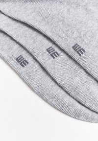 Szürke pamutzoknik sima textúrával. Az oldalán egy finom, sötétszürke logó minta található. Három pár sorba rendezve.