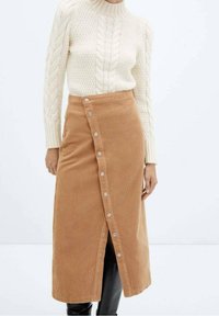 Gonna in corduroy color beige, lunga fino al ginocchio, con un'apertura frontale a bottoni e un design leggermente svasato, abbinata a un maglione in maglia a treccia color crema.