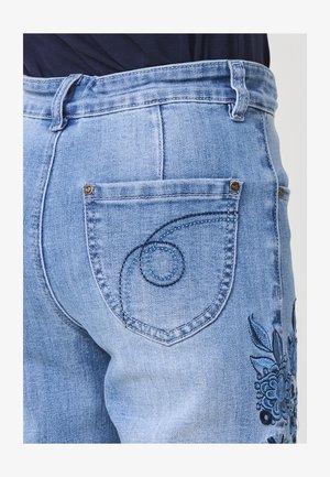 Jeans in denim azzurro chiaro con design floreale ricamato sul lato e motivo a spirale cucito sulla tasca posteriore.