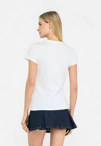 Hvid bomulds t-shirt med korte ærmer og rund hals, parret med en mørk denim plisseret nederdel med en kantlinje lige over mid-thigh.