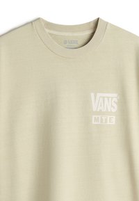 Lys beige løstsiddende t-shirt lavet af blødt bomuld med rund hals, med et hvidt Vans-logo og "MTE" trykt på brystet.