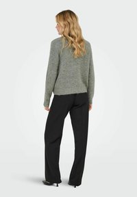 Suéter de punto gris claro con un ajuste relajado, con mangas largas y un dobladillo sin terminar, combinado con pantalones de traje negros y zapatos negros.