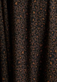 Leopardenmusterstoff mit einer Mischung aus schwarzen und orangefarbenen Punkten auf einem dunkelbraunen Hintergrund, der eine glatte, weiche Textur zeigt.