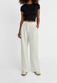 Zwart cropped T-shirt gecombineerd met witte wijde broeken met een trekkoord in de taille. Sneakers met groene en beige accenten maken de outfit compleet.