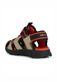 Sandalía beige y negra con acentos rojos, parte superior de malla, suela de goma y correas ajustables para un ajuste seguro. Marca GEox visible en el talón.