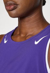 Fialová športovái top s okrúhlym výstrihom, s bielymi logami Nike na ramenách a hladkým, textúrovaným materiálom.