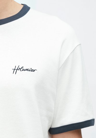 Fehér rövid ujjú póló sötétkék bordázott nyak- és ujjvégekkel, a mellkason apró hímzett logóval.