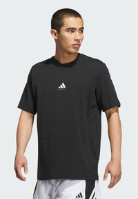 Camiseta negra de manga corta hecha de algodón con cuello redondo y un logo blanco de Adidas sobre la palabra "basketball" en el frente.