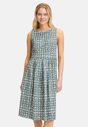 Ärmelloses grünes Kleid mit einem geometrischen Muster in Weiß, das einen taillierten Oberteil und einen gefalteten Rock bis zur Mitte der Wade hat.