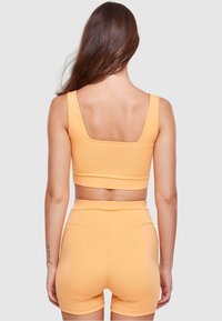 Elastisk orange sportset med en fyrkantig halsringning crop top och högsittande shorts. Slät textur, åtsittande design, minimala sömmar synliga.