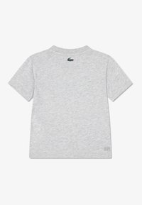 Γκρι κοντομάνικη μπλούζα από μαλακό ύφασμα βαμβακερού μείγματος. Διαθέτει στρογγυλή λαιμόκοψη και μικρό πράσινο λογότυπο κροκοδείλου στο πίσω μέρος.