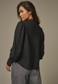 Blusa nera con tessuto testurizzato, maniche a sbuffo e inserti in pizzo sulle cuciture. Abbinata a jeans in denim grigio chiaro a vita alta.