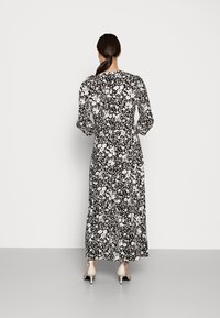 Robe maxi avec un motif floral noir et blanc, dotée de manches longues et d'une taille cintrée. Tissu lisse et design à longueur de cheville.