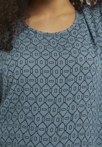 Blauw patroon shirt met een geometrisch ontwerp met zwarte omtrekken. Rund hals en zachte stof, met lichte plooien op de schouders.