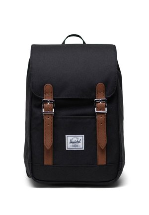 Zaino in tessuto nero con spallacci in pelle marrone e fibbie in metallo. Presenta una tasca frontale, un badge logo cucito e una maniglia superiore per il trasporto.