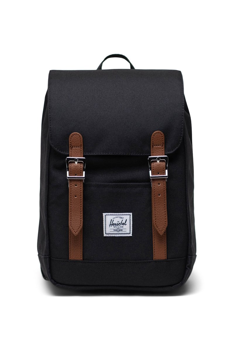 Czarny plecak z tkaniny z brązowymi skórzanymi paskami i metalowymi klamrami. Posiada przednią kieszeń, naszywkę z logo oraz uchwyt na górze do noszenia.