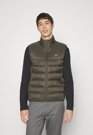 Green puffer vest with a high collar, featuring a front zipper and a small yellow logo on the chest, worn over a black long-sleeve shirt.