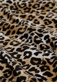 Tkanina s uzorkom leoparda koja ima meku teksturu s smešnim, crnim i kremasto-bijelim mrljama, s raznolikim oblicima i veličinama točkica.