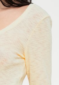 Ανοιχτό κίτρινο, υφασμένο πλεκτό τοπ με φαρδιά λαιμόκοψη και μακριά μανίκια, με σχέδιο πλέγματος και ελαφρά διαφάνεια.