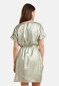 Short-sleeve, metallic green dress with a cinched waist. Smooth texture, featuring a keyhole back detail and a flowing A-line shape.