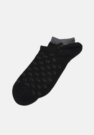 Chaussettes noires avec un motif répété de logo "CK" gris, un bord noir uni et un talon arrondi gris. Fabriquées à partir d'un mélange de tissus doux.