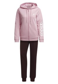 Sweat à capuche zippé Adidas rose clair avec logo sur la poitrine et la manche, associé à un pantalon de survêtement noir ajusté.