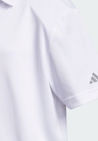Biała koszulka polo z krótkim rękawem z małym szarym logo Adidas na lewym rękawie, pokazana z bliska na jasnym tle.