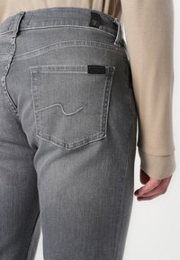 Gray denim jeans featuring a classic cut, subtle whiskering, and a distinctive embroidered back pocket accent. Tag visible on waistband.