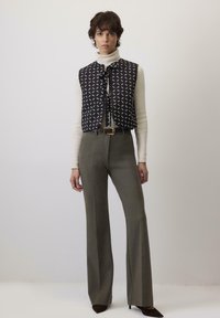 Prsluk s crno-bijelim uzorkom i mašnom, preko kreme turtleneck majice, u kombinaciji s maslinastozelenim širokim hlačama i smeškim potpeticama.