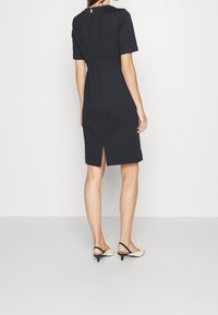 Robe noire ajustée avec manches courtes, fermeture éclair au dos et longueur mi-mollet. Comprend une fente centrale au dos et une texture lisse.