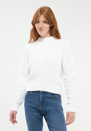 Maglione bianco lavorato a maglia con colletto alto e motivo a trecce, con orli a coste e maniche lunghe, abbinato a jeans blu.