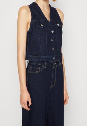 Ærmeløs mørk denimvest med knapper, båret med matchende mørke denimbukser, med forlommer og kontrastsyningsdetaljer.