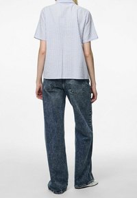 Camicia a maniche corte in cotone azzurro chiaro e bianco a righe, abbinata a jeans blu sbiaditi a vestibilità ampia, che mostrano una silhouette rilassata.