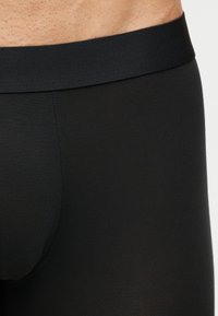 Κοντινό πλάνο ενός ατόμου που φοράει μαύρα εφαρμοστά σορτς με ελαστική μέση, δείχνοντας τη μέση και την περιοχή του άνω μηρού.