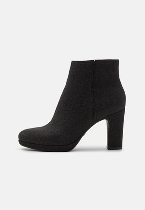 Bottine noire en tissu texturé, à bout rond, avec fermeture éclair sur le côté et talon large sur un fond blanc.