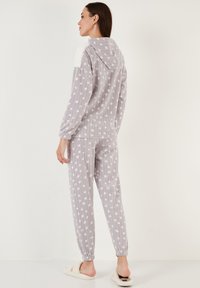 Šedý loungewear set obsahující mikinu s kapucí a jemným bílým akcentem a vzorem s puntíky, doplněný o kalhoty s elastickým pasem ve stejném designu.