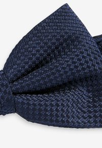 Papillon intrecciato di colore blu navy con un motivo a quadri testurizzato e un centro annodato. Il materiale sembra liscio e ben cucito.