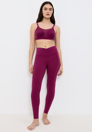 Fioletowy sportowy biustonosz z regulowanymi ramiączkami oraz dopasowane legginsy z wysokim stanem, z geometrycznymi przeszyciami i gładką fakturą.