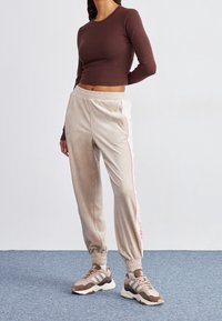 Hnědý dlouhý rukáv top spárovaný se světle béžovými tepláky s růžovými bočními pruhy. Nosit s hnědými teniskami, což vytváří sportovní vzhled.