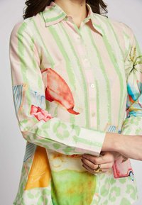 Kleurvol overhemd met knopen, dat een mix van pastelstrepen, abstracte patronen en levendige illustraties op een lichte stof toont.