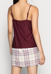 Bordeaux tanktop met dunne bandjes bij de halslijn, gecombineerd met een geruite beige rok met paarse en roze lijnen.
