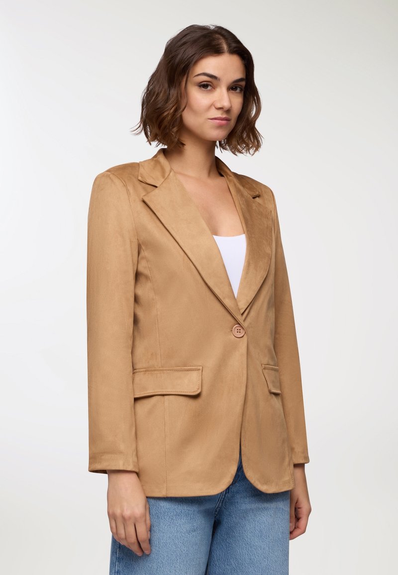 Blazer in suede beige con chiusura a un bottone, rever a punta e due tasche frontali. Texture morbida e design strutturato.